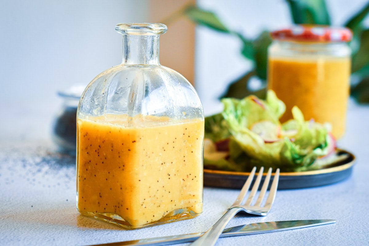 A jar of dressing next to a salad and fork.