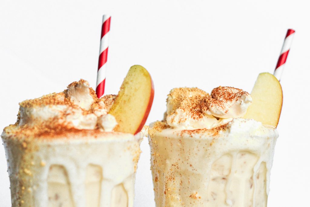 Apple pie milkshake with a straw and apple slices.