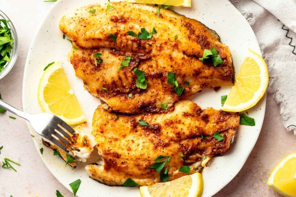 Grilled fish fillets on a plate with lemon slices.