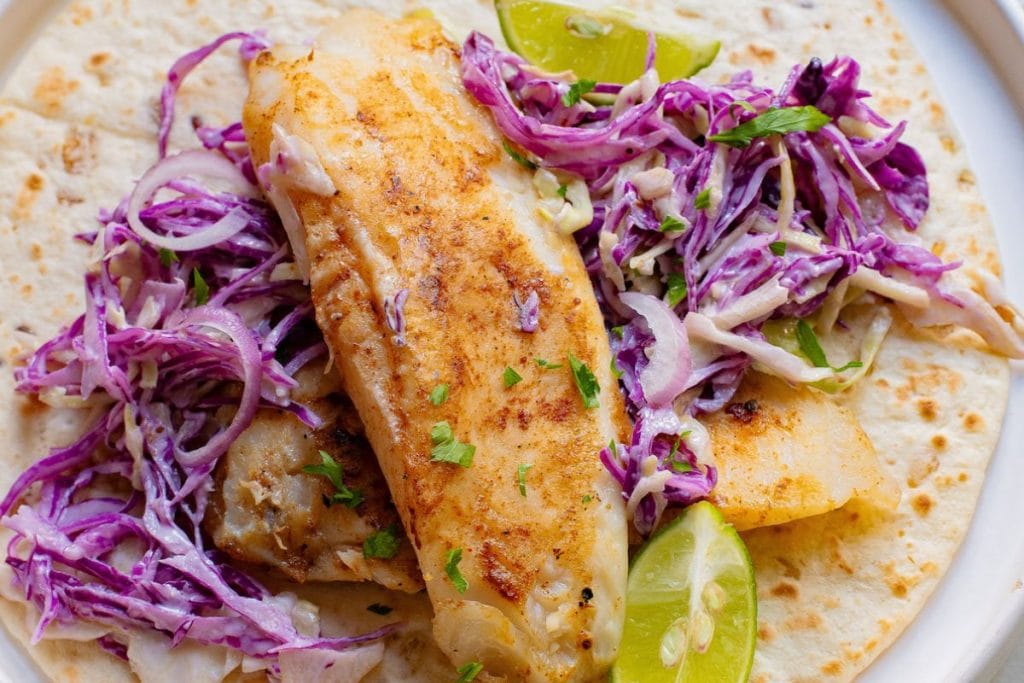 Fish tacos with cabbage slaw and lime wedges.