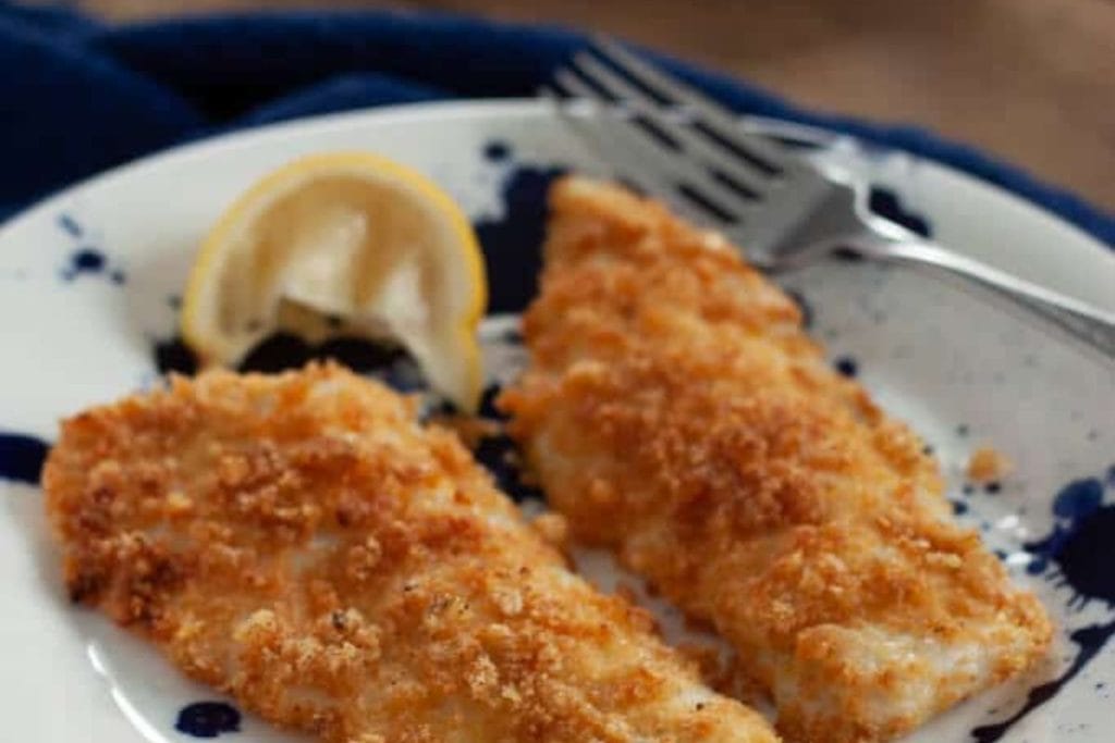 Fried fish fillets on a plate with lemon wedges.