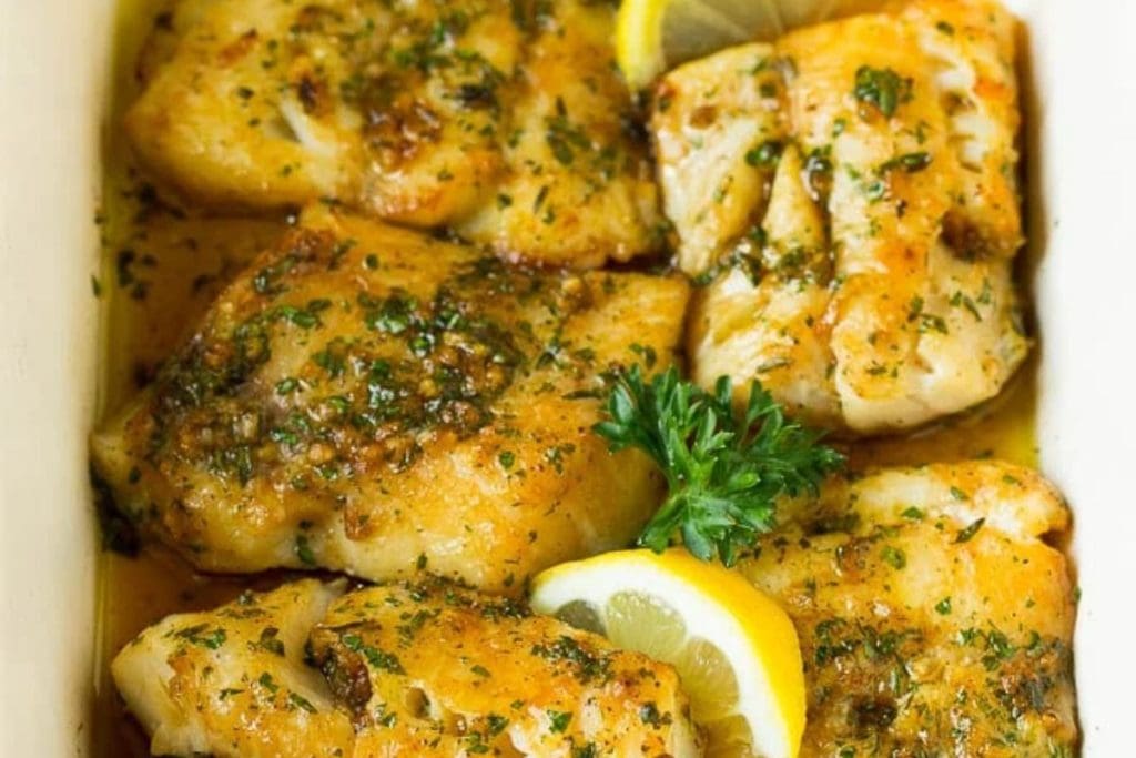 Fish fillets in a white baking dish with lemon and parsley.