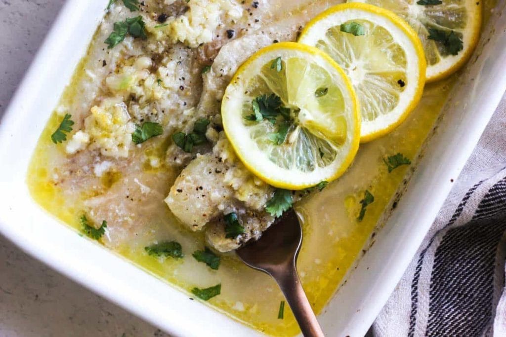 A white dish with lemons and fish in it.