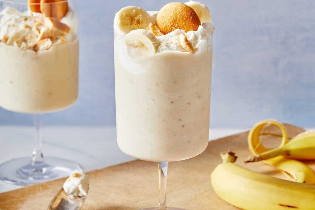 Two glasses of banana milkshake with whipped cream and bananas.