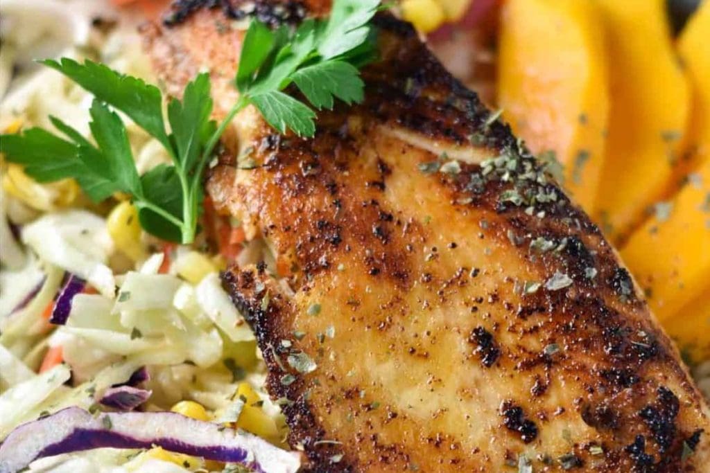 A plate of grilled salmon with a side of coleslaw and mangoes.