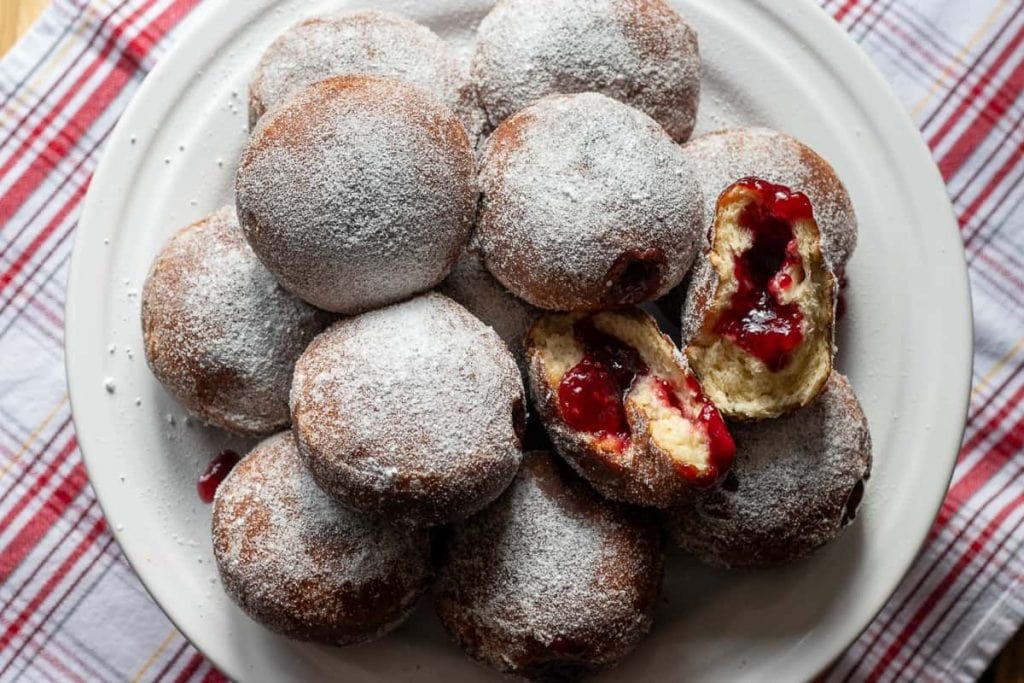 A plate of donuts with jam and powdered sugar.