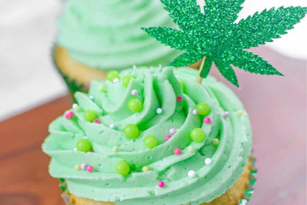 Two green cupcakes with a marijuana leaf on top.