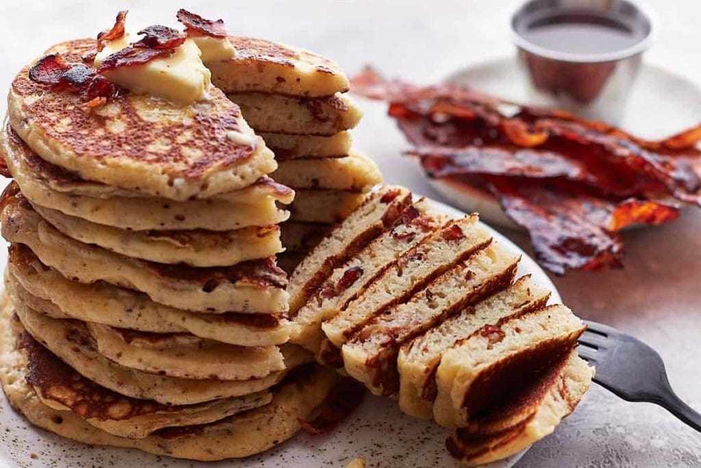 A stack of pancakes with bacon and butter on a plate.