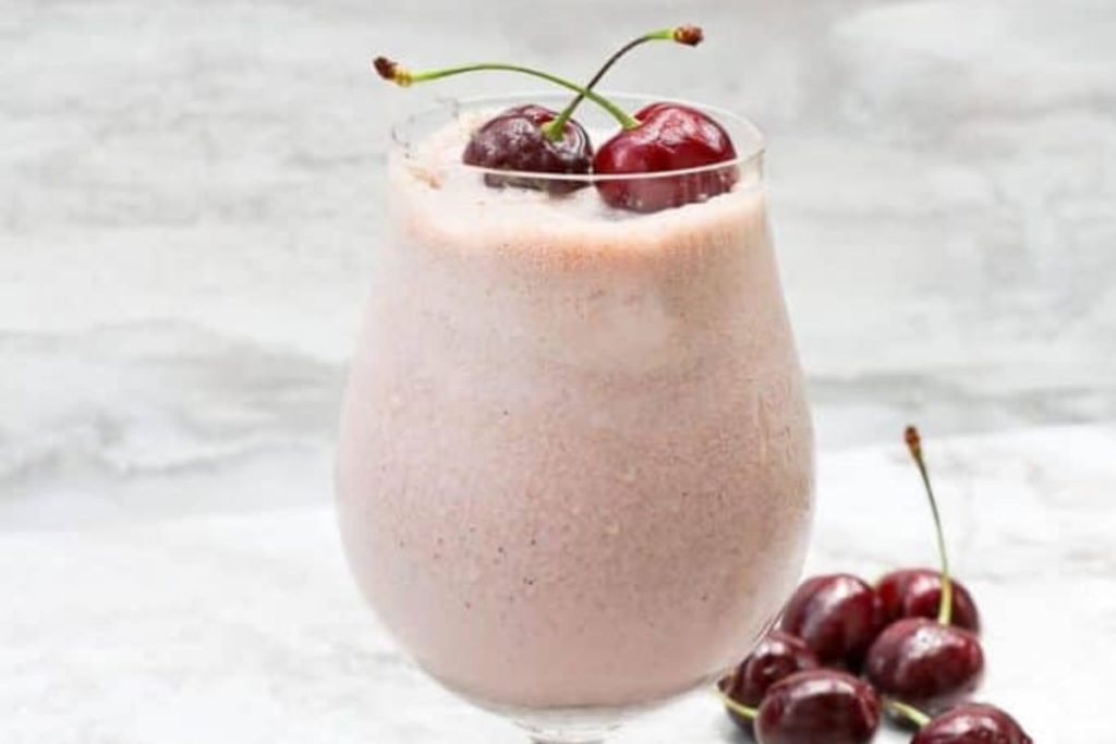 A cherry smoothie in a glass with cherries on top.