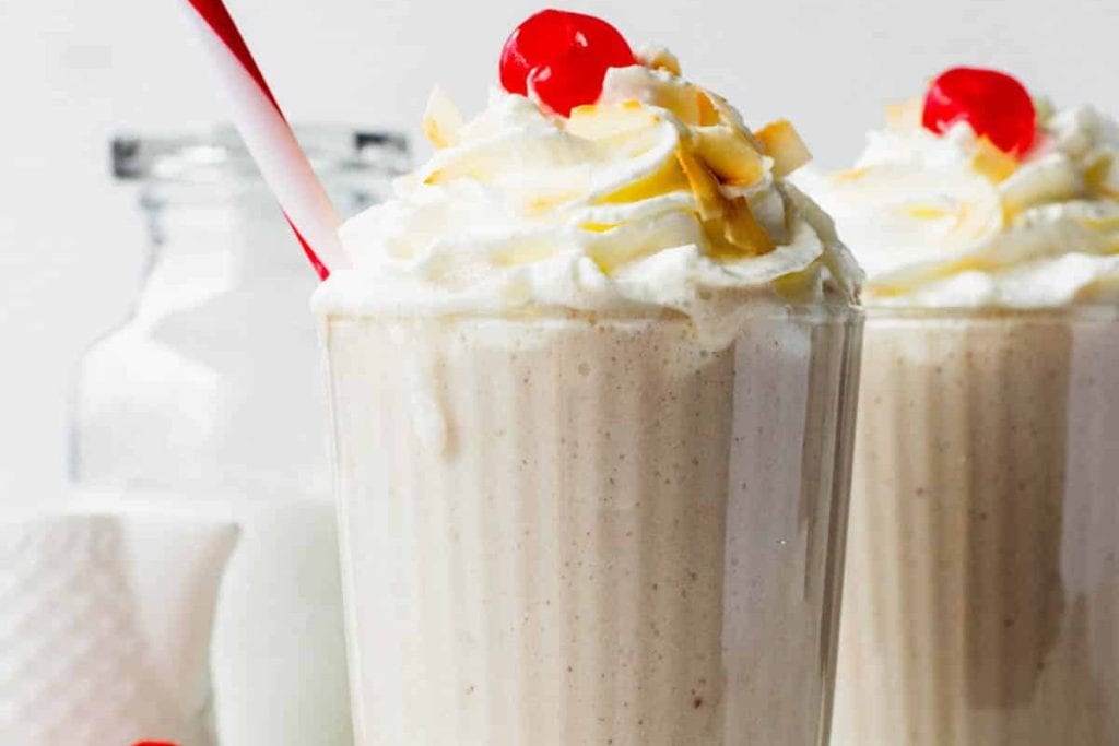 Two milkshakes with whipped cream and a cherry on top.