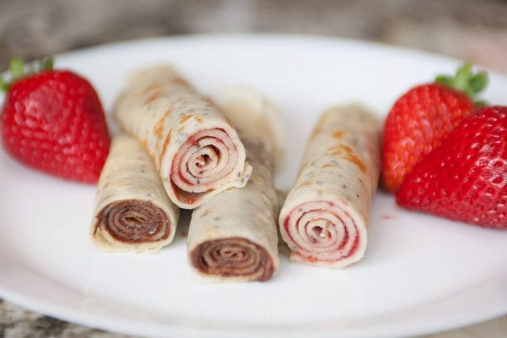 Chocolate strawberry crepes on a plate with strawberries.