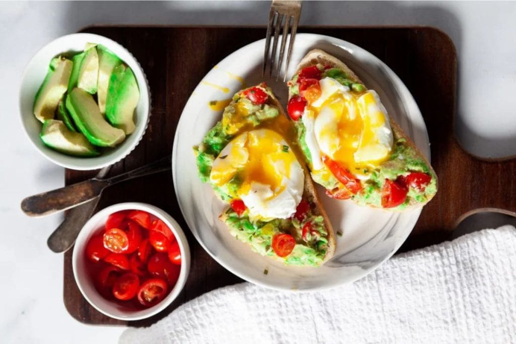 Avocado toast with eggs and tomatoes on a cutting board.
