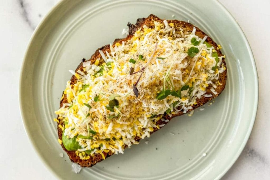 A plate of toast with cheese and greens on it.