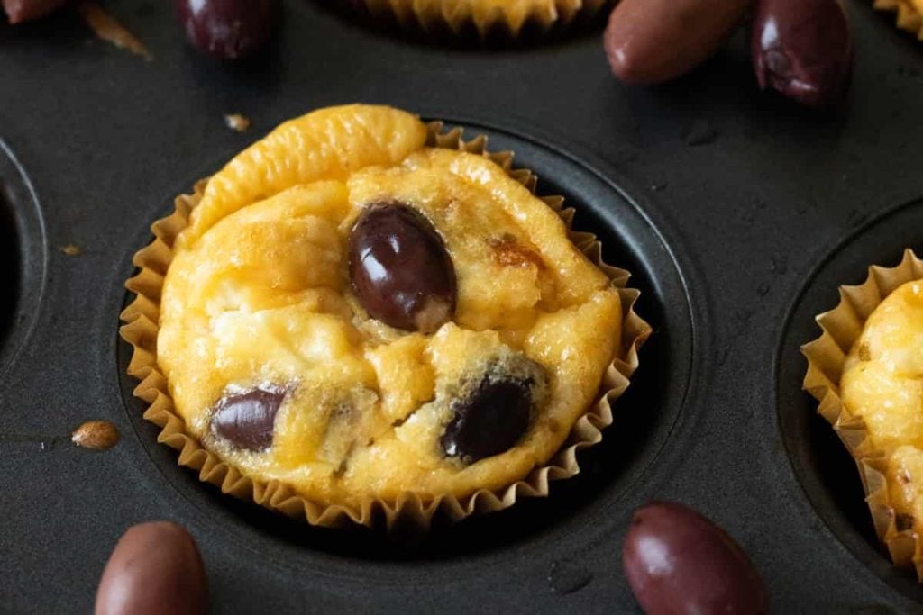 A muffin tin filled with muffins and olives.