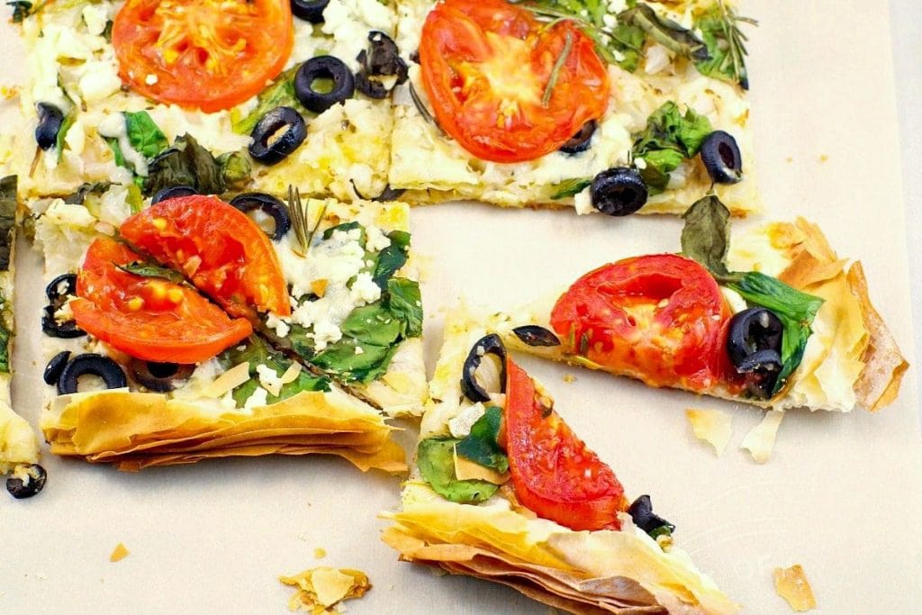 A pizza with tomatoes, olives, and basil.