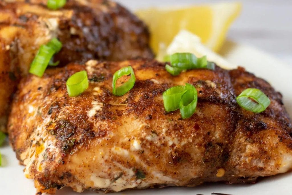 Two pieces of fish on a plate with lemon wedges.