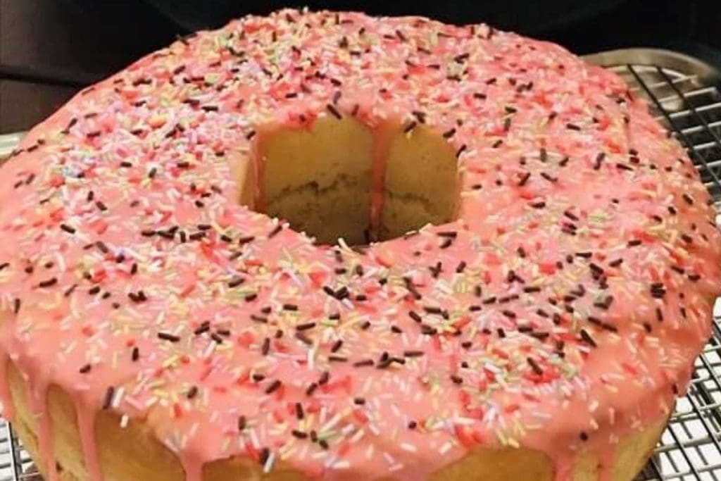 A pink donut cake with sprinkles on top.