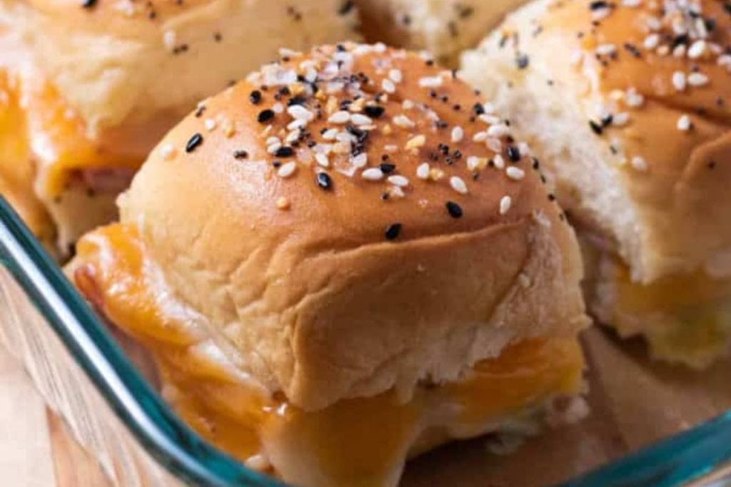Ham and cheese sliders in a glass dish with sesame seeds.