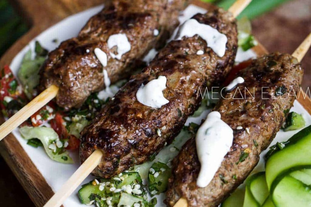 Kebabs on skewers with cucumbers and sour cream.
