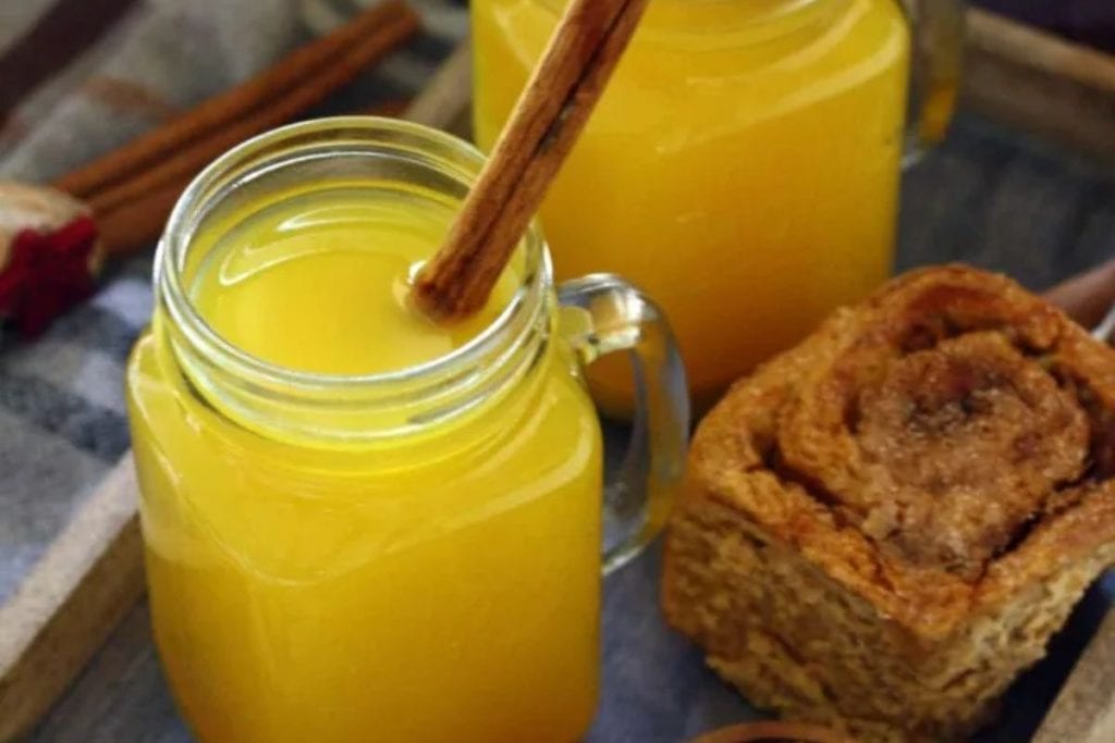 Two jars of orange juice with cinnamon sticks on a tray.