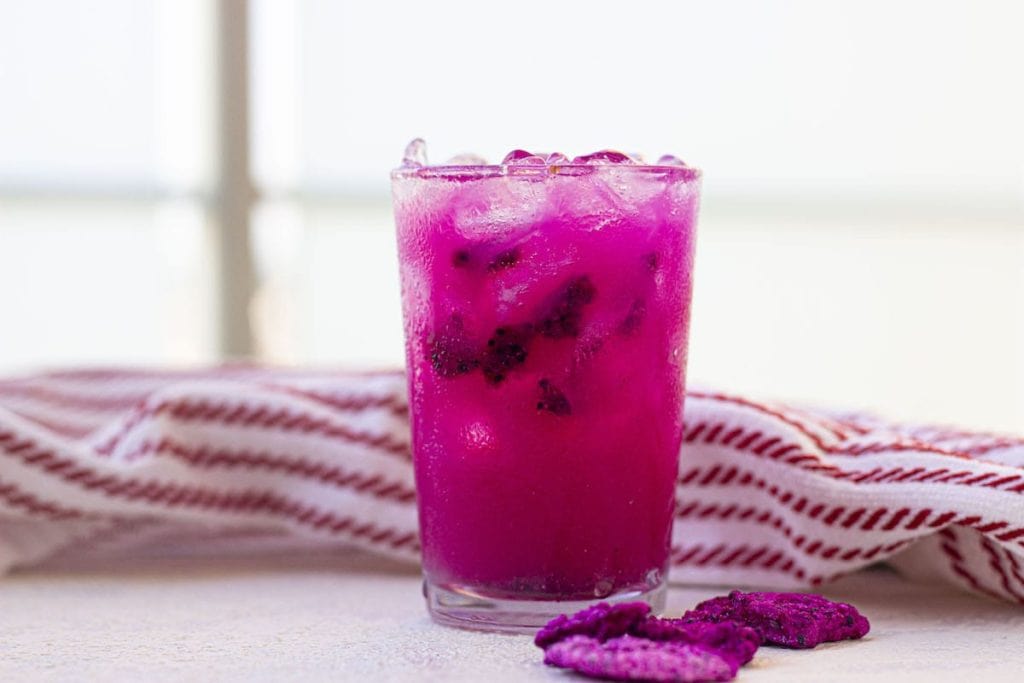 A pink drink with ice and berries on a table.
