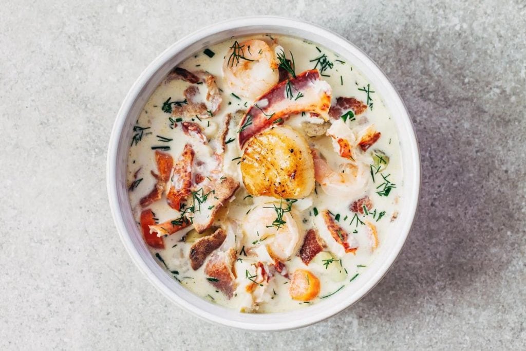 A bowl of seafood chowder with shrimp and bacon.