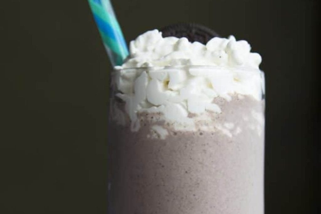 An oreo milkshake with whipped cream and a blue straw.