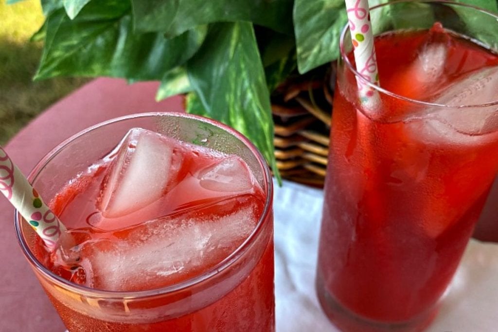 Two glasses of strawberry lemonade with ice and straws.