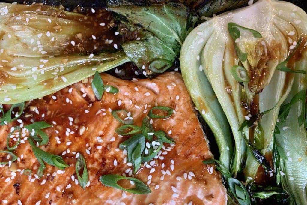 A tray of salmon and vegetables with sesame seeds.