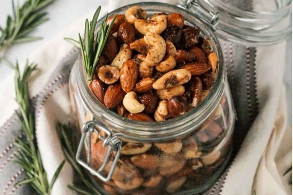Nuts in a glass jar with rosemary sprigs.