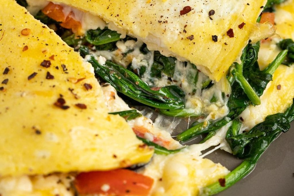 A close up of an omelet with spinach and tomatoes.