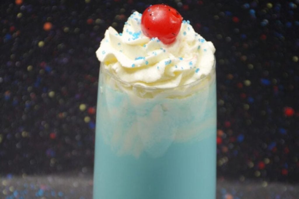A blue drink with whipped cream and a cherry on top.