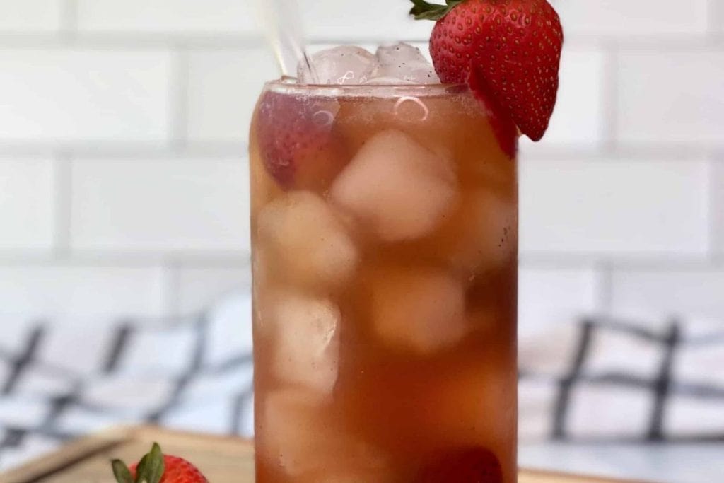 A tall glass of iced tea with strawberries on top.
