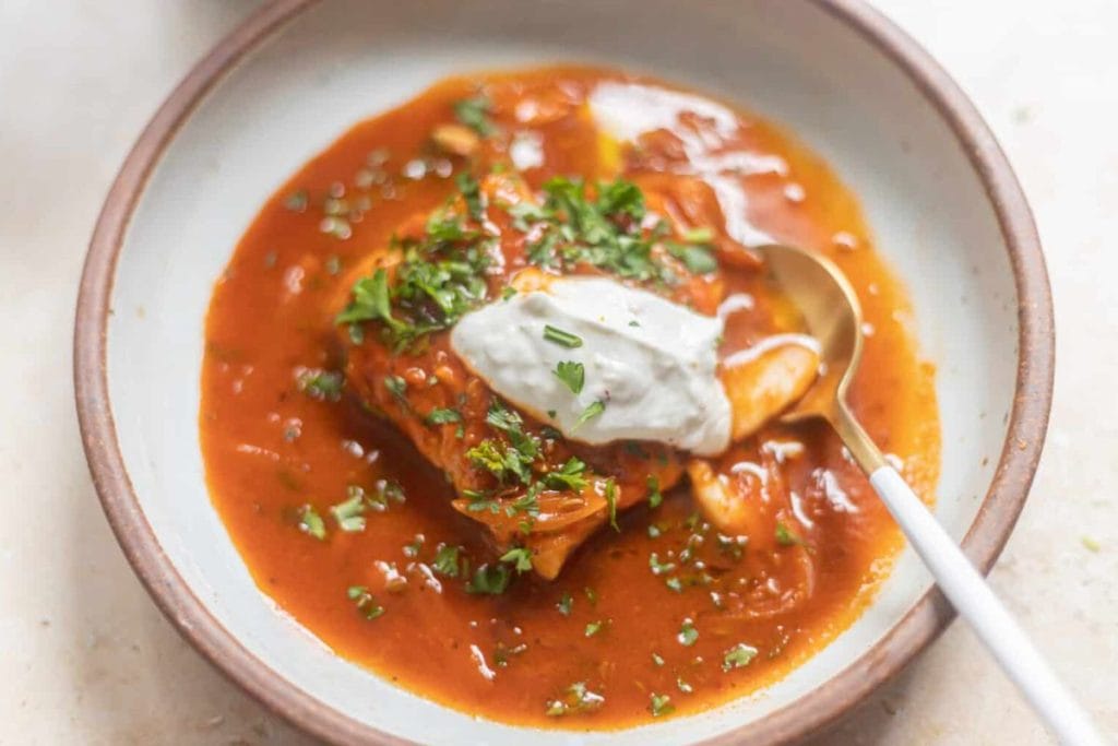 A bowl of stew with sour cream and a spoon.