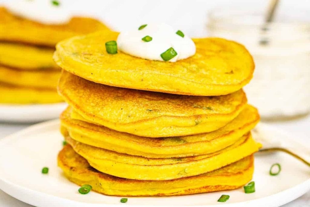 A stack of pumpkin pancakes with sour cream and green onions.