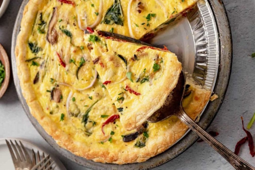 A quiche with spinach and mushrooms on a plate.