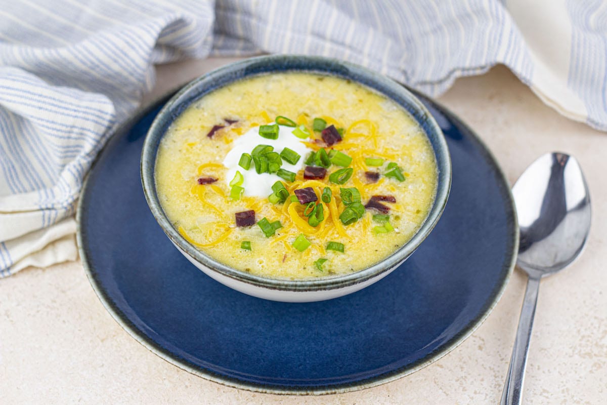 Bowl of creamy hash brown potato soup topped with shredded cheese and herbs.