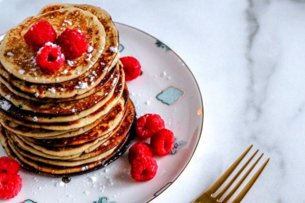 A stack of pancakes with raspberries on a plate.