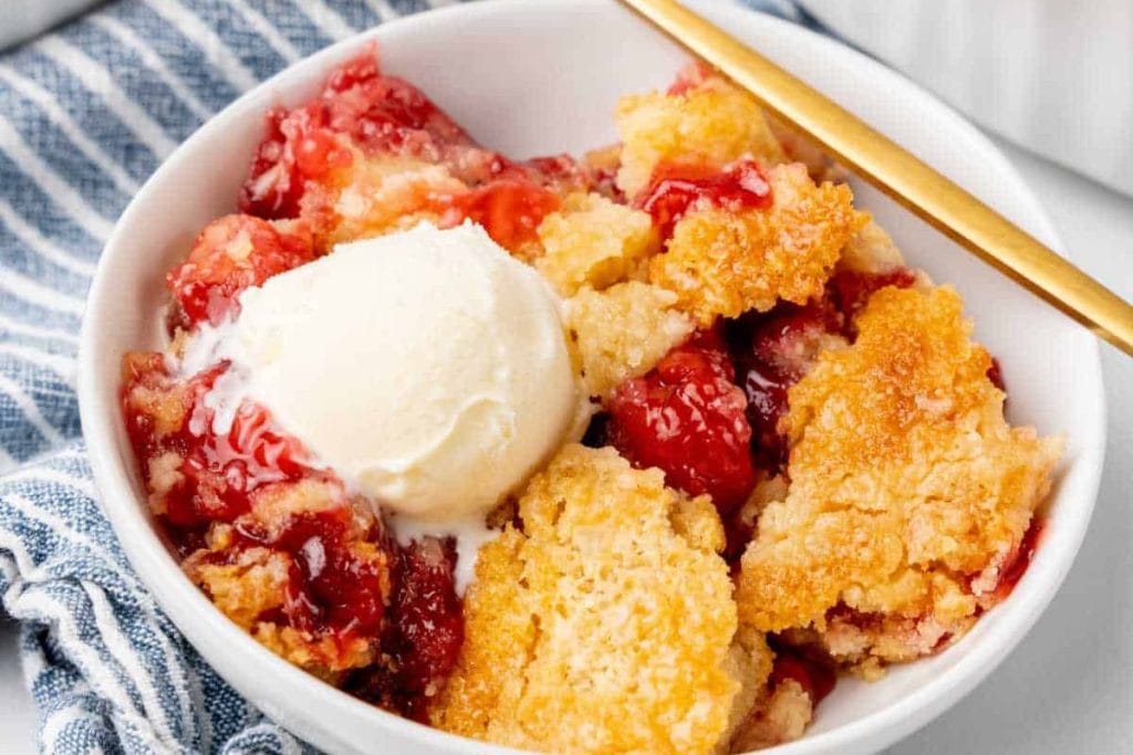 Last-Minute Potluck Idea: Strawberry cobbler topped with a scoop of ice cream, served in a white bowl.