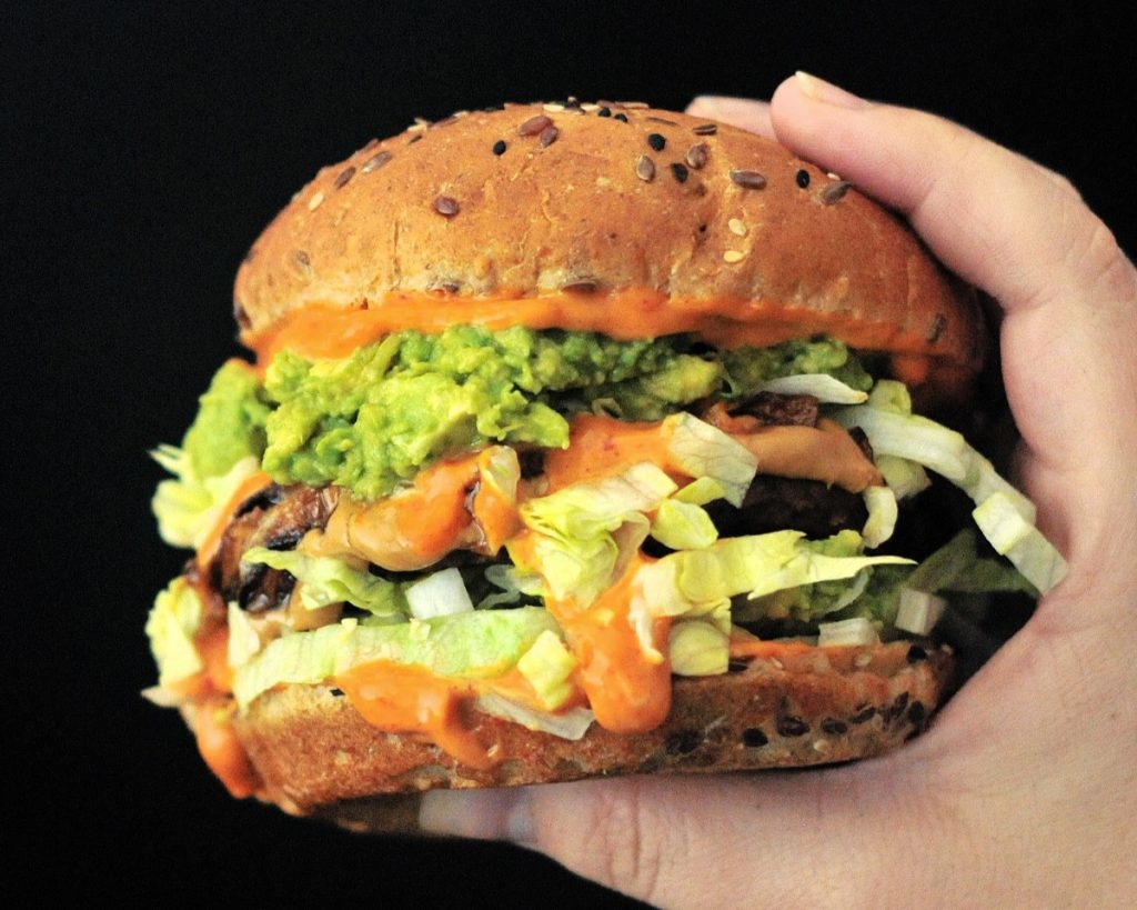 A person holding a burger with guacamole on it.