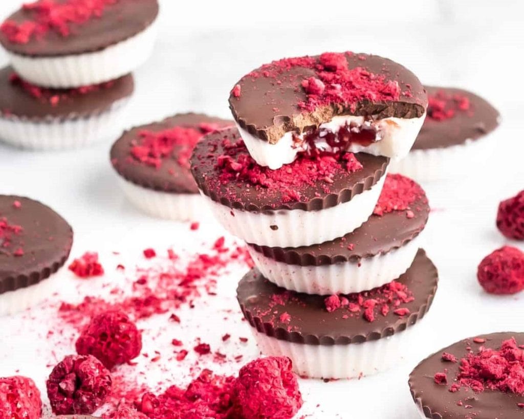 Healthy chocolate-covered mini cheesecakes with a raspberry topping, some cut in half to reveal the filling.