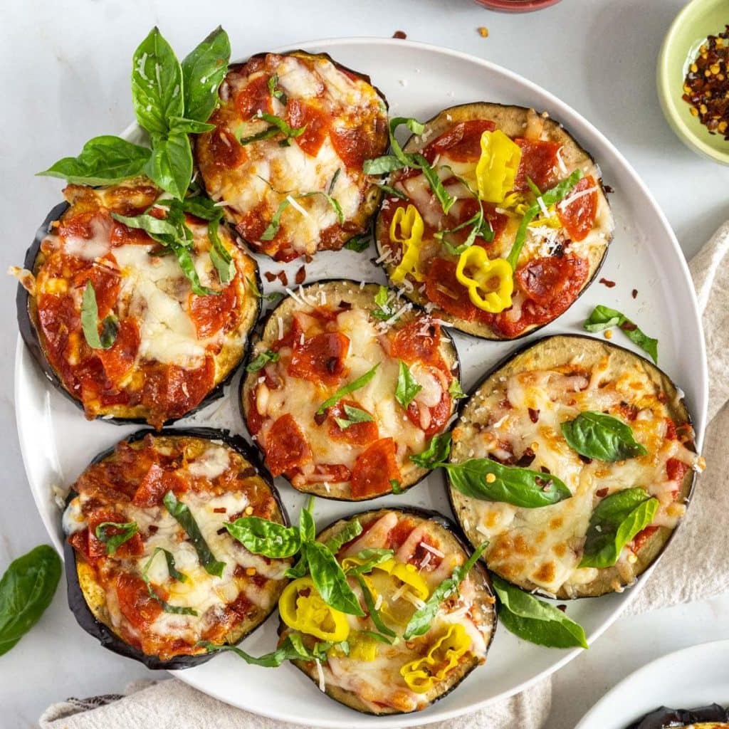 A plate of healthy snacks featuring baked eggplant slices topped with tomato sauce, melted cheese, and basil.