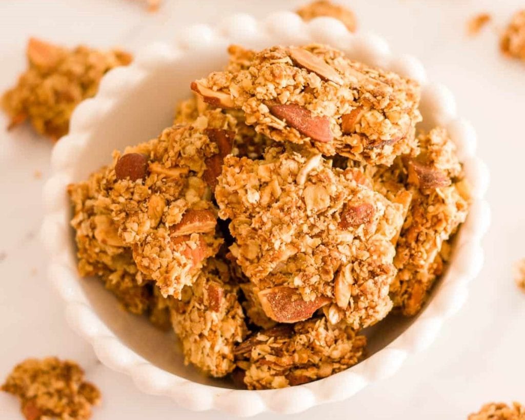 A bowl of healthy almond granola bars on a white surface.