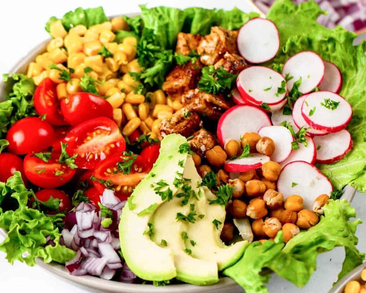 A colorful salad bowl perfect for last-minute dinner ideas, with lettuce, tomatoes, chickpeas, avocado, radishes, corn, and seasoned chicken.