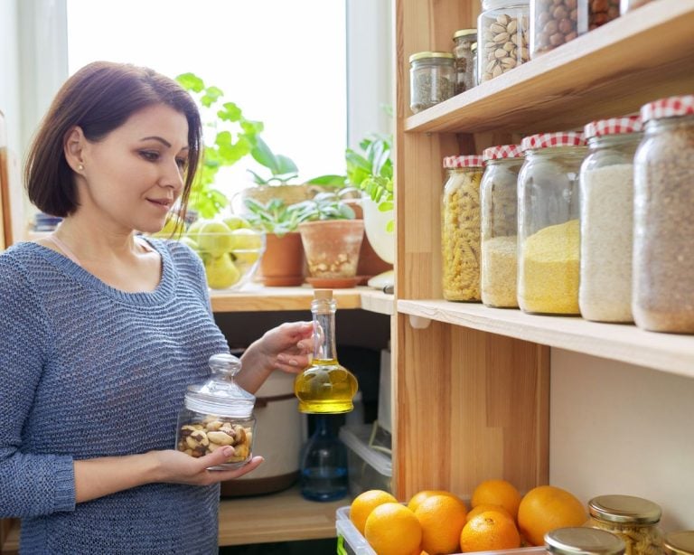 Woman organizing kitchen cabinet with jars of dry goods for organization ideas.