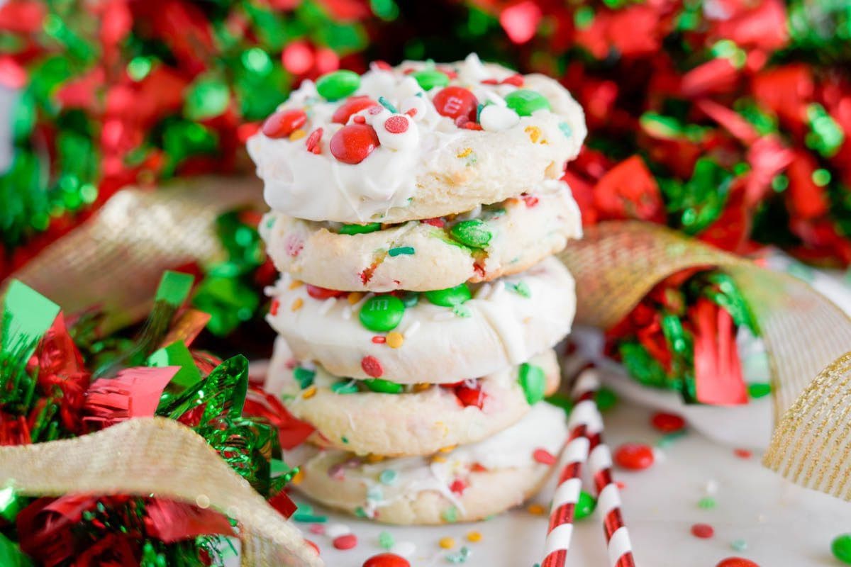 A stack of festive cookies with white icing and colorful candies, surrounded by red and green holiday decorations, perfect for your favorite Christmas cookie recipes.