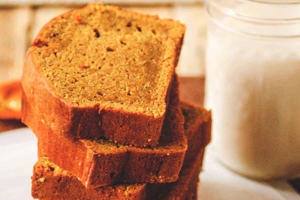 Three slices of pumpkin bread stacked on a plate next to a glass of milk.