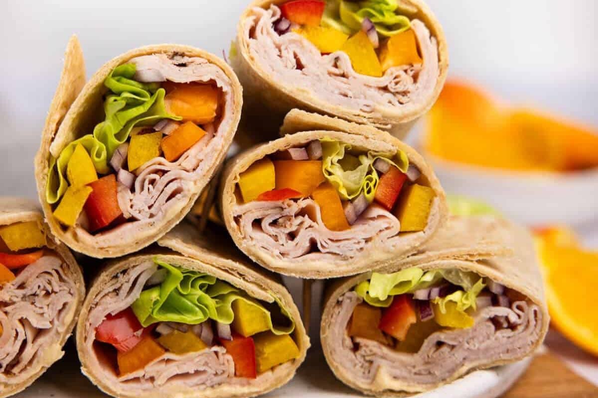 Close-up of fresh vegetable and turkey wraps, filled with sliced bell peppers, lettuce, and turkey slices, arranged on a white plate.