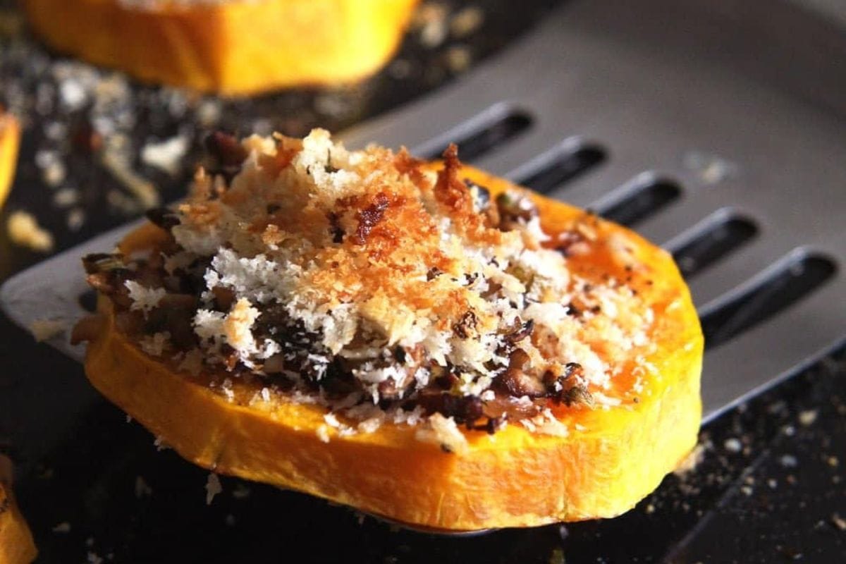 Close-up of a slice of roasted butternut squash topped with breadcrumbs and herbs on a spatula, perfect for your favorite roasted butternut squash recipes.