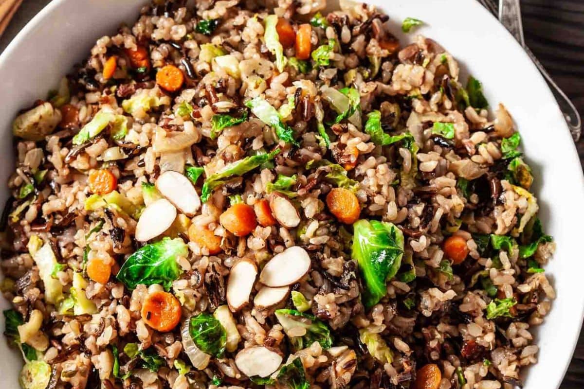 A bowl of rice salad with almonds, Brussels sprouts, carrots, mushrooms, and other mixed vegetables.